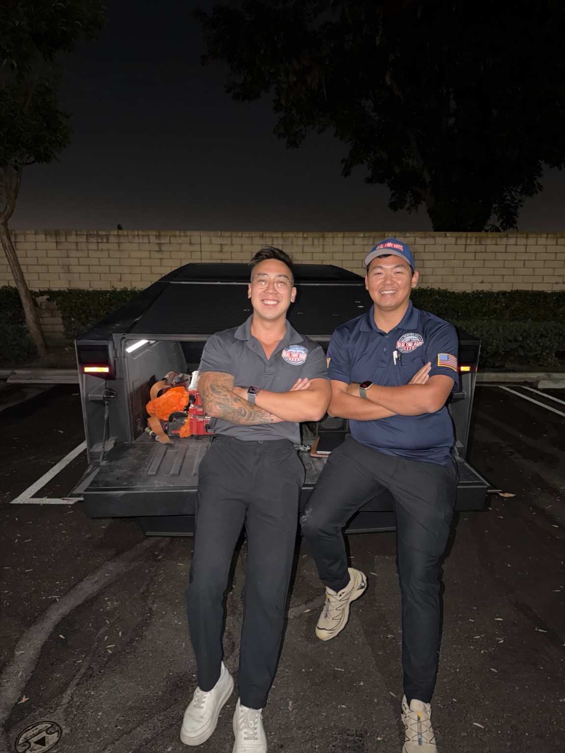 Andrew and Alvin in Real Time Bros uniforms, standing together at the back of their truck